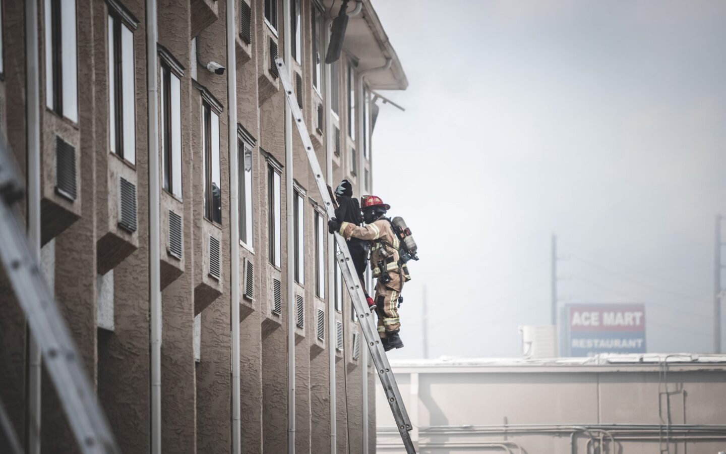 Two firefighters in full gear climb a ladder to reach an upper floor of a building during an emergency response.