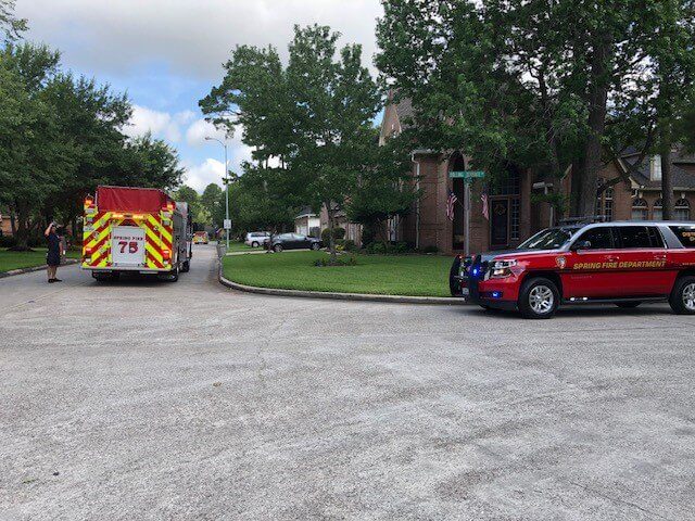A fire truck and a Spring Fire Department SUV are parked on a suburban street near houses with trees and grass visible.