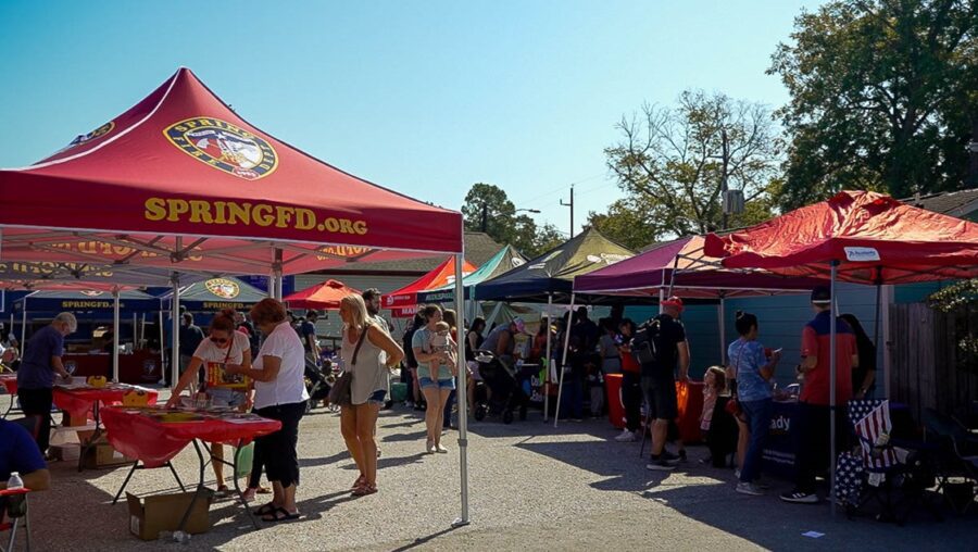 People gather at an outdoor event with various red tents and tables, including one labeled "SPRINGFD.ORG," on a sunny day.