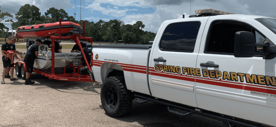 A Spring Fire Department truck tows a rescue boat on a trailer, with firefighters standing nearby preparing equipment.
