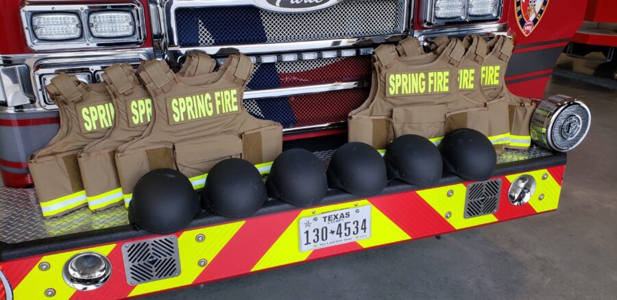 Five tactical vests labeled "Spring Fire" and five black helmets are displayed on the front bumper of a fire truck with a Texas license plate.