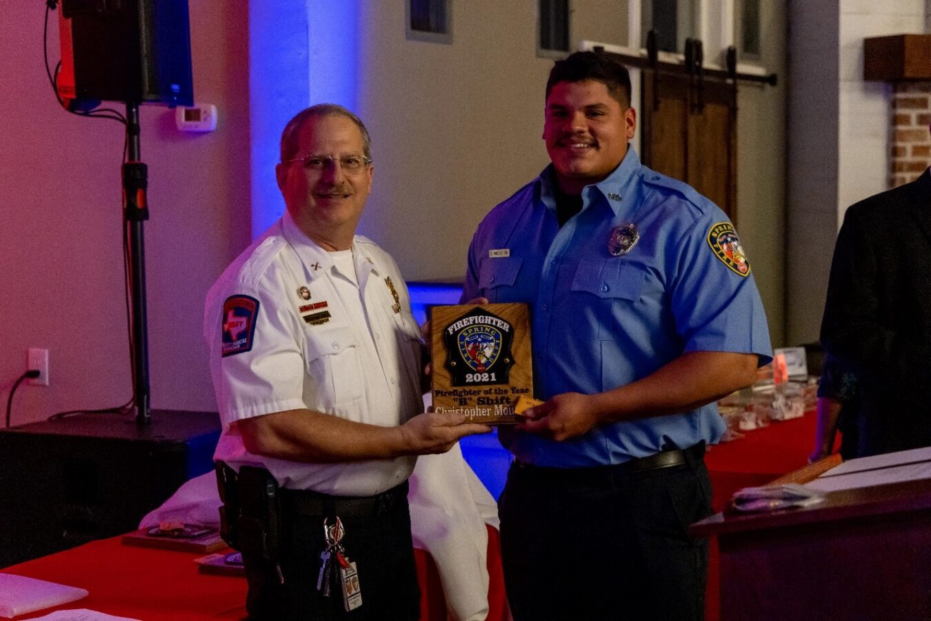 Two uniformed men at an indoor event, one handing the other a plaque that reads "2021 Responder of the Year, Firefighter Mitchell.