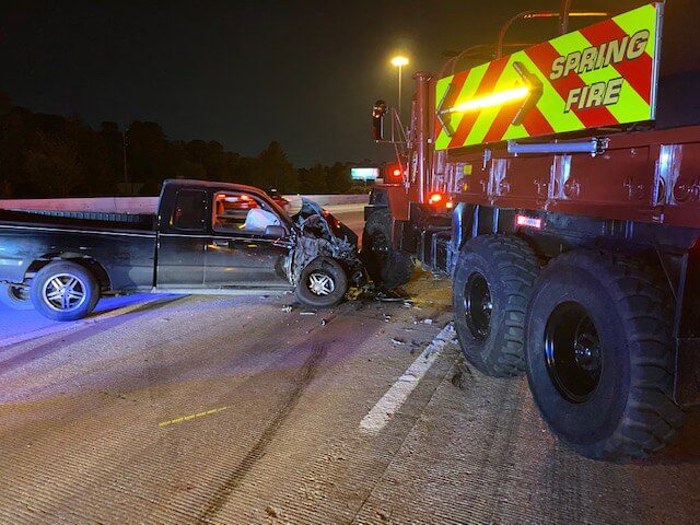 A black pickup truck has collided head-on with a large fire truck labeled "Spring Fire" on a highway at night.