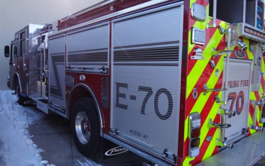 A red and silver fire truck labeled "E-70" is parked outside on a snowy surface. The rear of the truck has high-visibility yellow and red stripes.