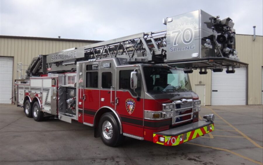 A red and silver fire truck with an extended ladder is parked outside a beige industrial building with roll-up doors.