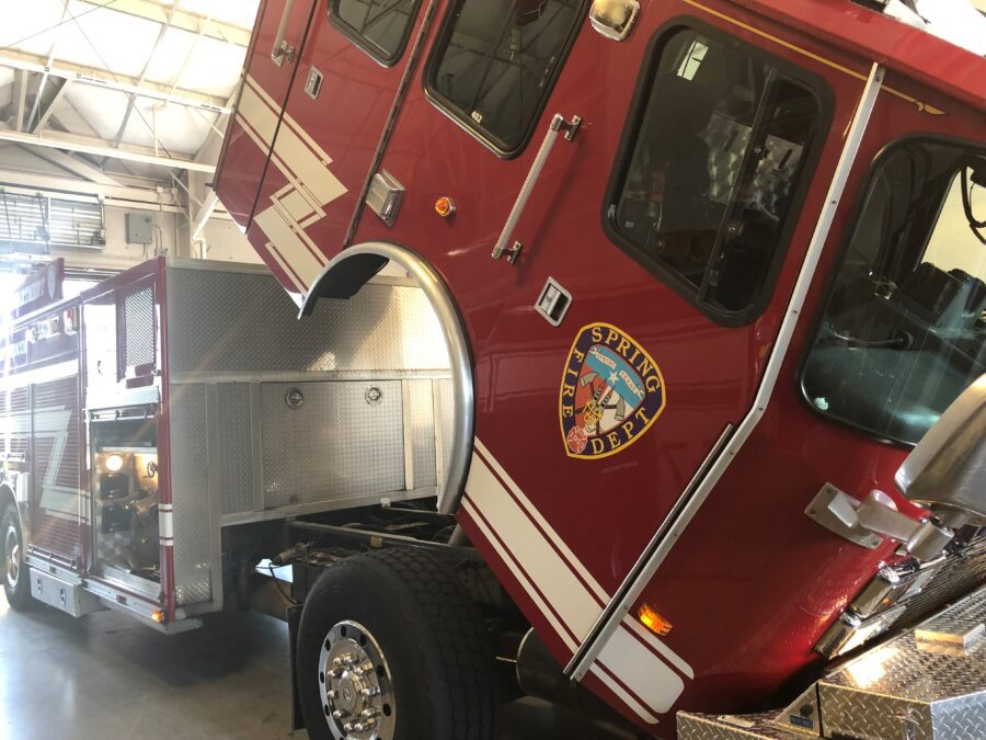 A red fire truck with its cab tilted forward is parked inside a garage; the "Spring Dept" emblem is visible on the door.