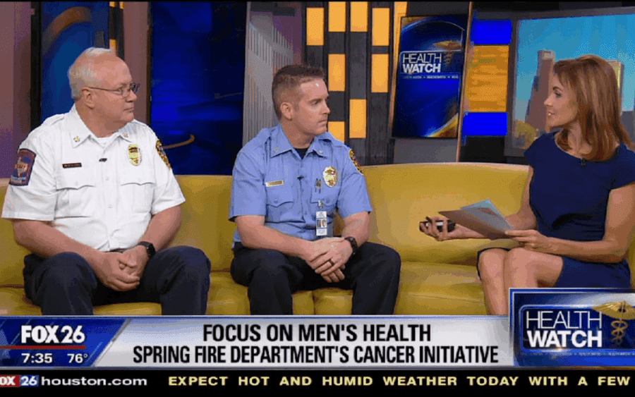 Two fire department officials and a news anchor sit on a yellow couch discussing men's health and a cancer initiative on FOX 26's Health Watch segment.