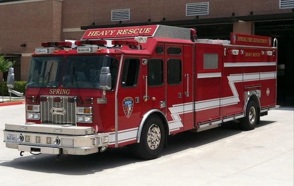 A red heavy rescue fire truck labeled "Spring" is parked outside a fire station building.