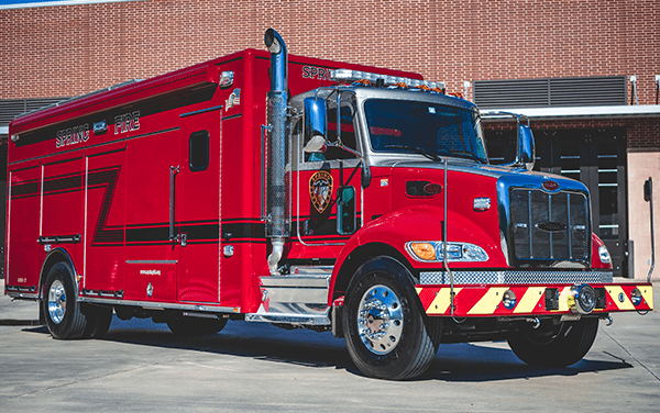 A large red fire rescue truck is parked outside a brick building on a sunny day.