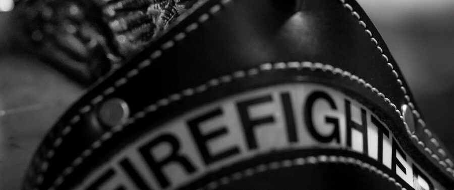 Close-up, black-and-white image of a firefighter’s helmet showing the word "FIREFIGHTER" with visible stitching details.