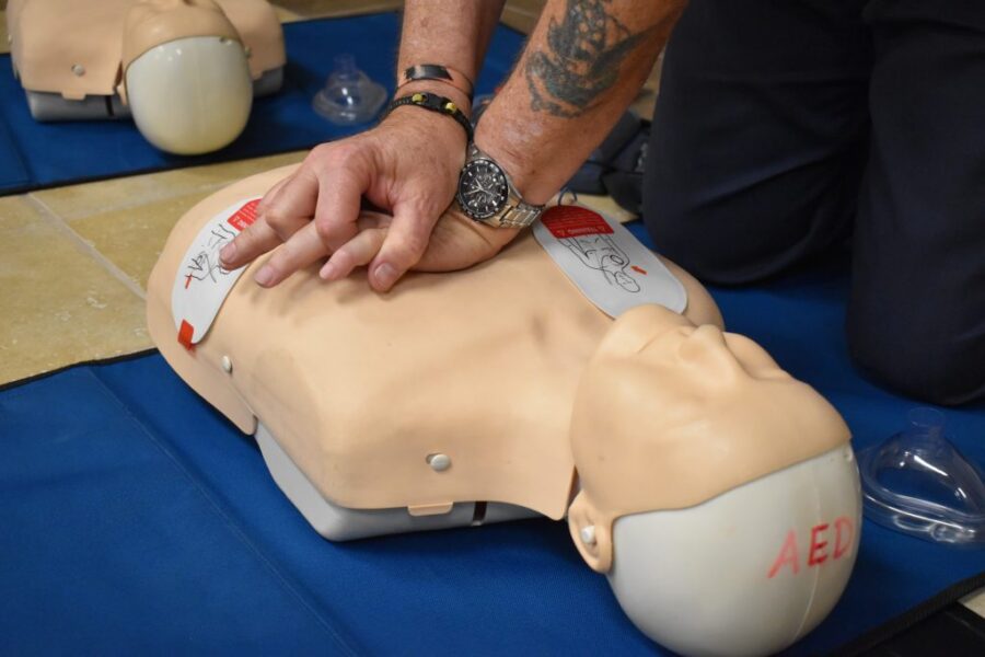 Person practicing chest compressions on a CPR training manikin labeled "AED" placed on a blue mat.